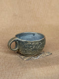 Textured stoneware cup with cratered surface and pale blue glaze inside, Ripples collection