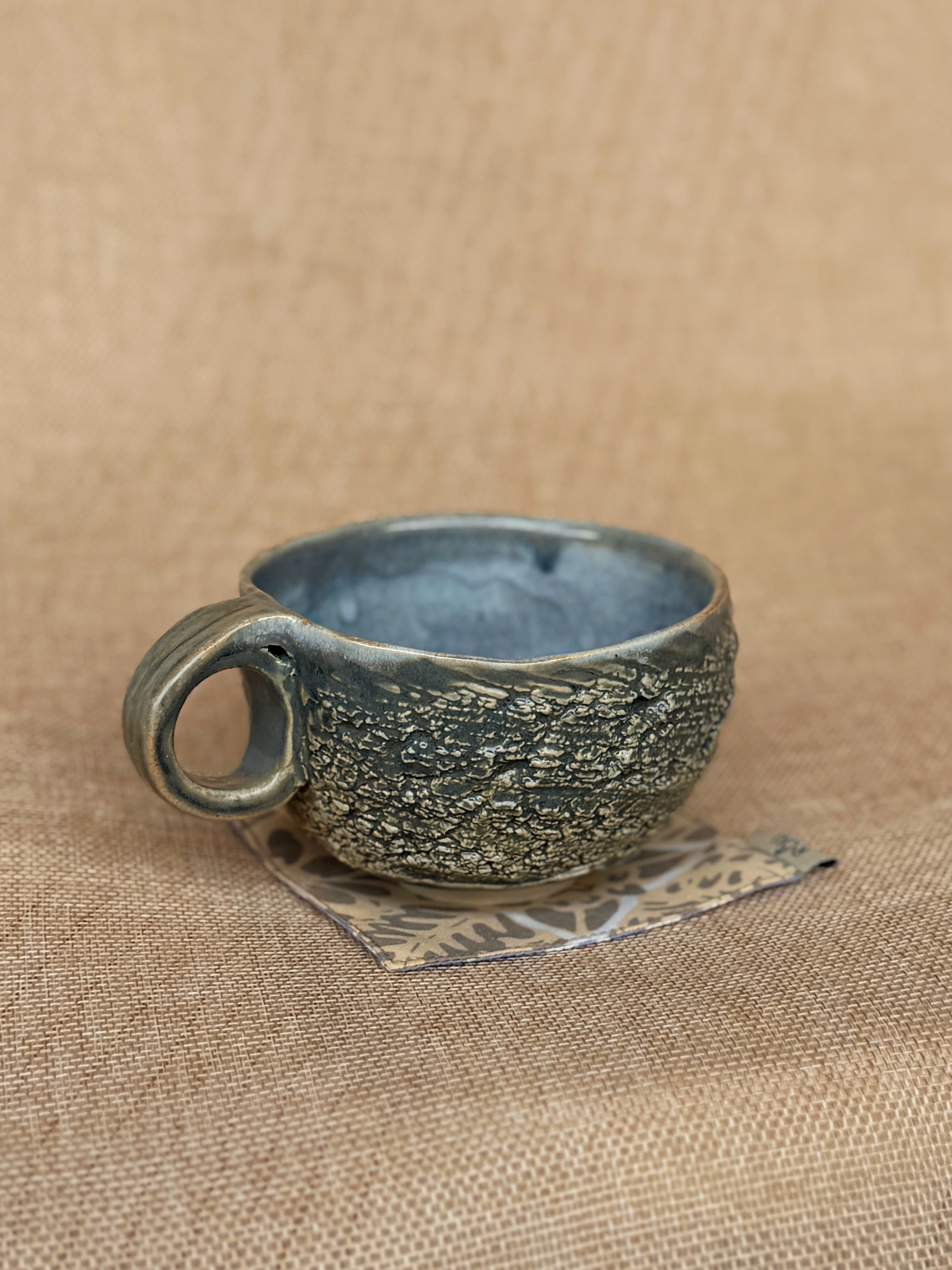 Textured stoneware cup with cratered surface and pale blue glaze inside, Ripples collection
